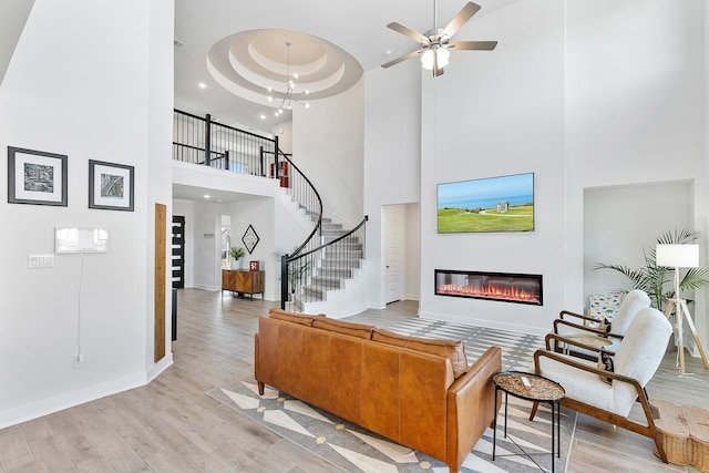 living room with a towering ceiling, a tray ceiling, ceiling fan with notable chandelier, and light wood-type flooring