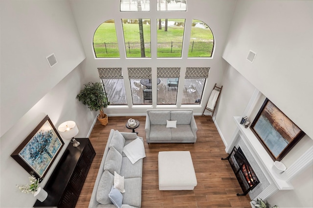 living room with visible vents, a lit fireplace, a high ceiling, and wood finished floors