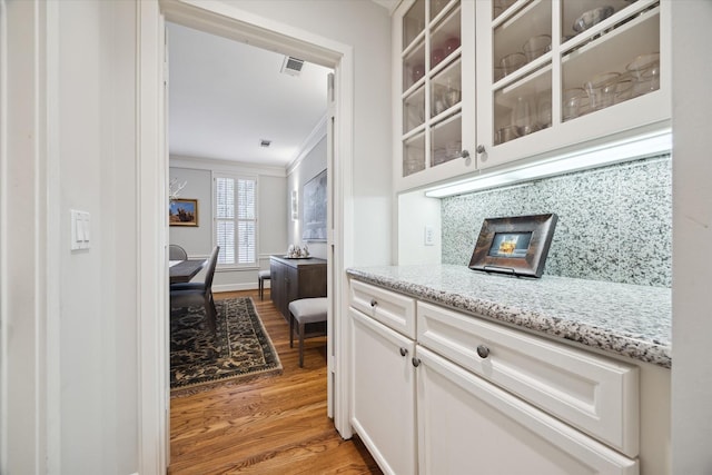 kitchen with light hardwood / wood-style flooring, tasteful backsplash, white cabinetry, light stone countertops, and ornamental molding