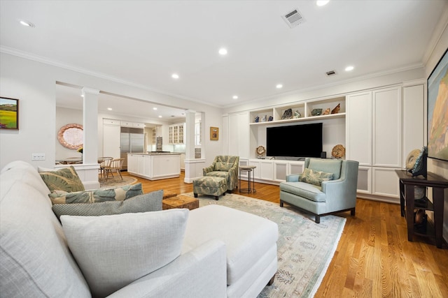 living room featuring decorative columns, crown molding, and light wood-type flooring