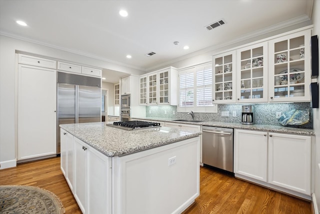 kitchen with sink, white cabinetry, built in appliances, and a kitchen island