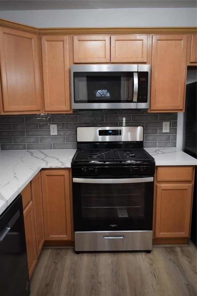 kitchen with tasteful backsplash, appliances with stainless steel finishes, light stone countertops, and hardwood / wood-style floors