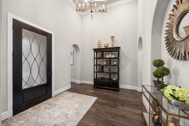 entryway featuring arched walkways, dark wood-type flooring, a notable chandelier, and baseboards