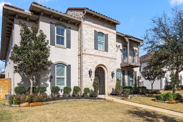 mediterranean / spanish-style house with a balcony, stone siding, a tile roof, a front lawn, and stucco siding