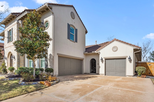 mediterranean / spanish home featuring an attached garage, driveway, stone siding, a tiled roof, and stucco siding