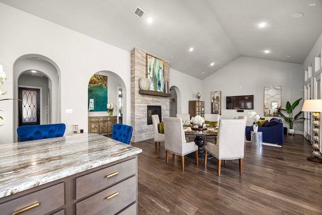 dining area featuring a stone fireplace, vaulted ceiling, and dark hardwood / wood-style floors