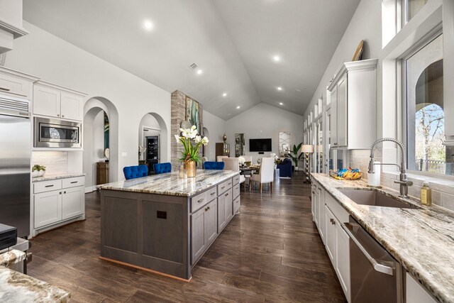 kitchen featuring lofted ceiling, sink, light stone counters, built in appliances, and white cabinets