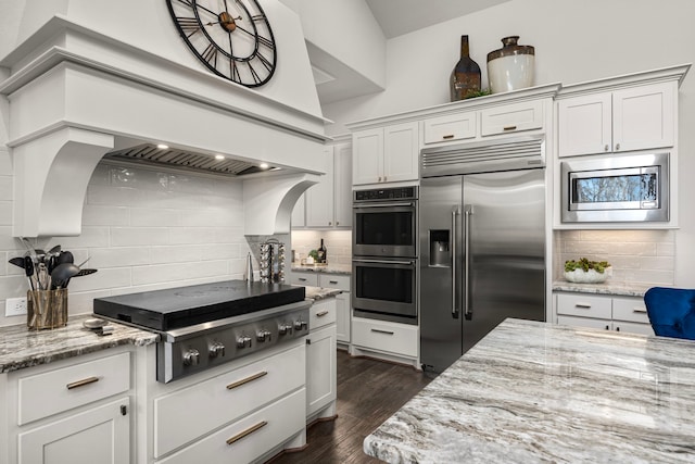 kitchen featuring dark wood-type flooring, white cabinetry, built in appliances, light stone counters, and tasteful backsplash