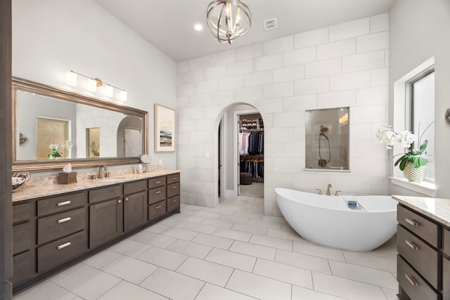 bathroom with tile walls, a soaking tub, a spacious closet, vanity, and tile patterned flooring