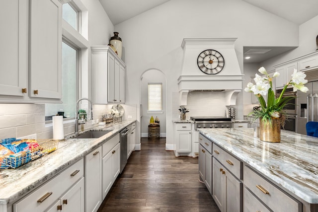 kitchen with dark wood finished floors, white cabinets, light stone countertops, stainless steel dishwasher, and a sink