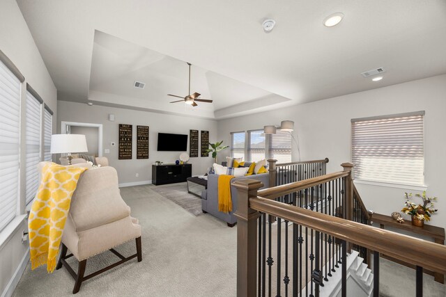 living room featuring a raised ceiling, light carpet, and ceiling fan