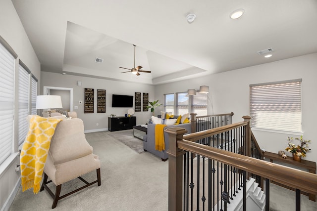 living area with baseboards, a tray ceiling, visible vents, and light colored carpet