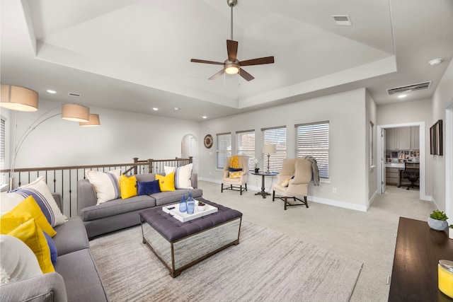 carpeted living room with a raised ceiling and ceiling fan