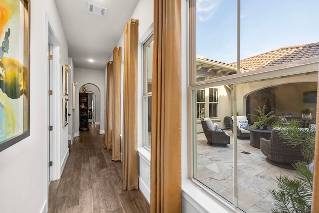 corridor featuring baseboards, visible vents, arched walkways, and wood finished floors