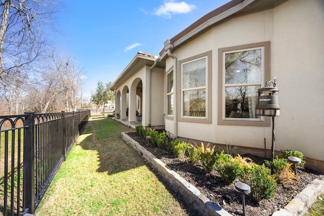 view of side of property with fence, a lawn, and stucco siding