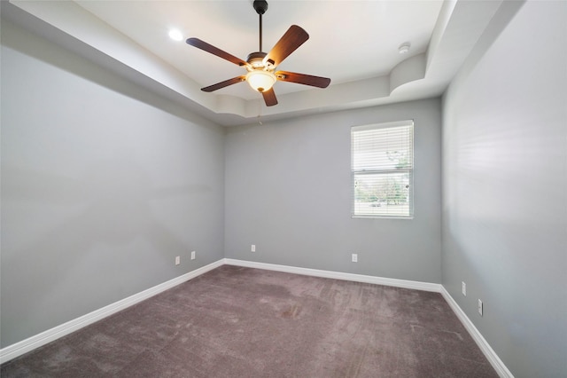 spare room featuring ceiling fan, a tray ceiling, and dark carpet