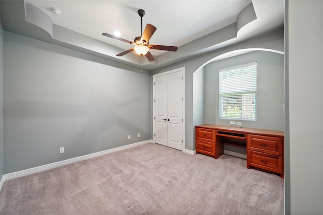 unfurnished bedroom with a raised ceiling, light colored carpet, and ceiling fan