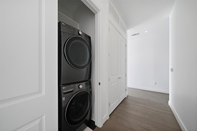 washroom with hardwood / wood-style flooring and stacked washing maching and dryer