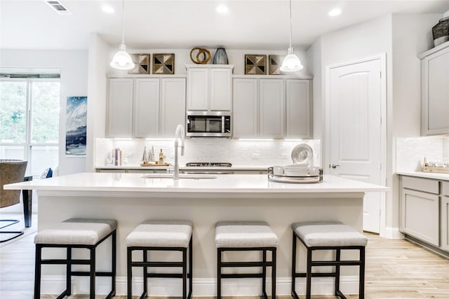 kitchen featuring sink, decorative light fixtures, a kitchen island with sink, and a breakfast bar