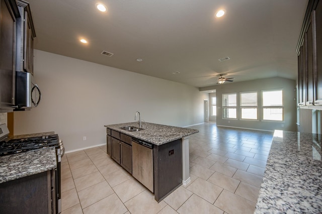 kitchen featuring sink, stainless steel appliances, light stone counters, an island with sink, and dark brown cabinetry