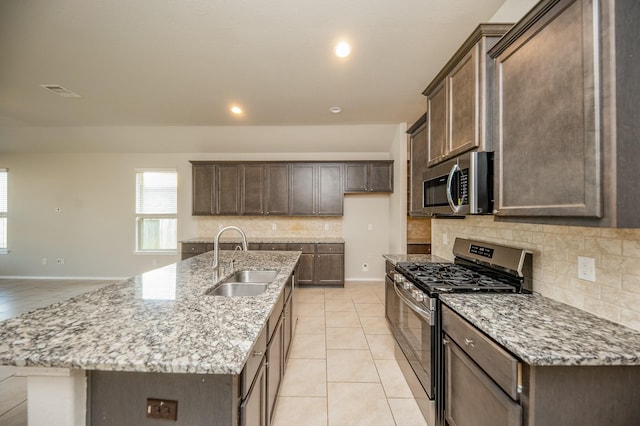 kitchen with dark brown cabinets, appliances with stainless steel finishes, sink, light stone countertops, and a kitchen island with sink