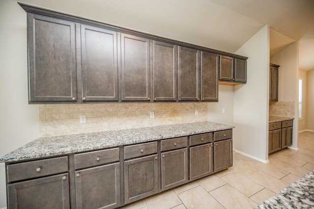 kitchen with backsplash, light tile patterned floors, light stone counters, lofted ceiling, and dark brown cabinetry