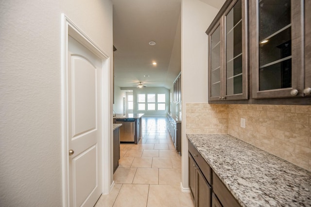 kitchen with light stone countertops, tasteful backsplash, light tile patterned floors, stainless steel dishwasher, and dark brown cabinets