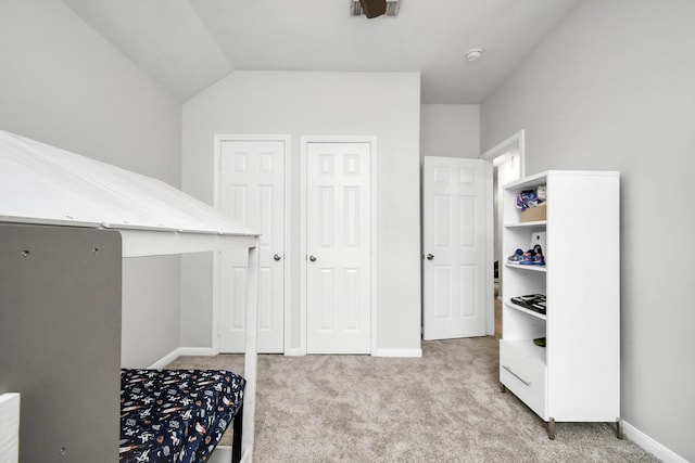 bedroom with light carpet, multiple closets, and vaulted ceiling