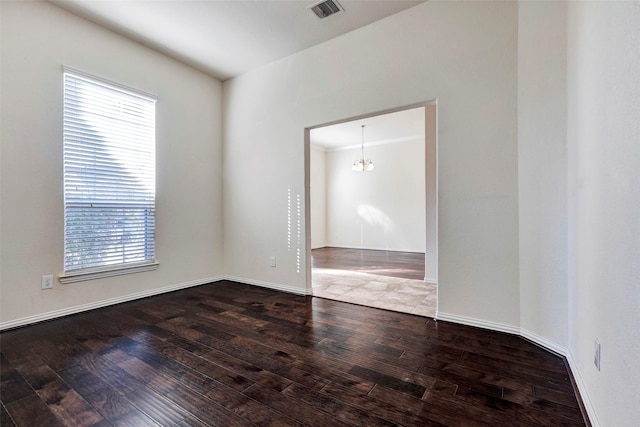 spare room with plenty of natural light, wood-type flooring, and a chandelier