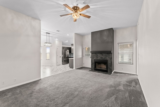 unfurnished living room with ceiling fan, a tile fireplace, and dark colored carpet