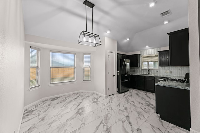 kitchen with light stone countertops, lofted ceiling, decorative backsplash, hanging light fixtures, and black fridge