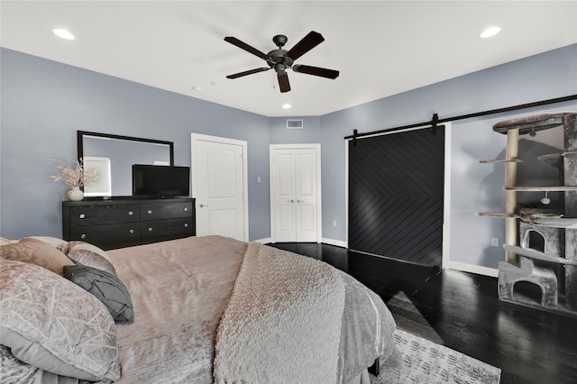 bedroom with a barn door, dark wood-type flooring, and ceiling fan