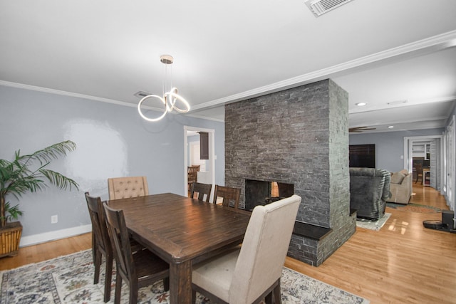 dining space featuring a notable chandelier, hardwood / wood-style flooring, ornamental molding, and a fireplace