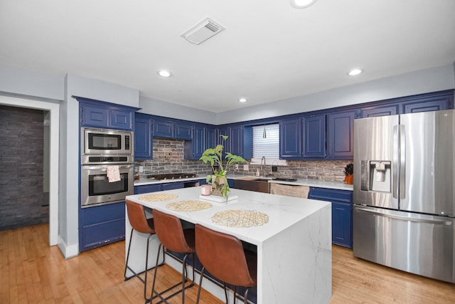 kitchen with a center island, blue cabinetry, appliances with stainless steel finishes, and a kitchen bar