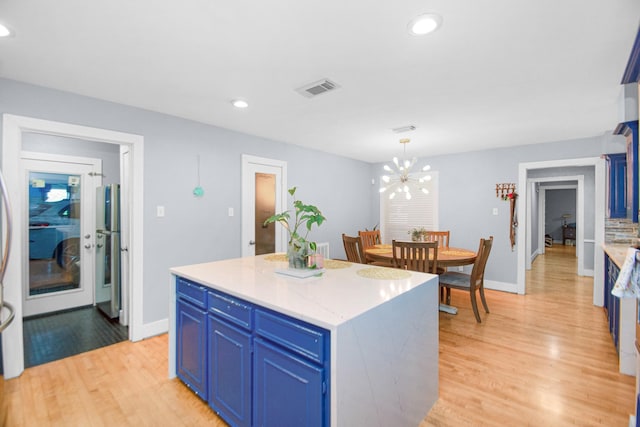 kitchen featuring decorative light fixtures, blue cabinetry, a center island, and light hardwood / wood-style flooring