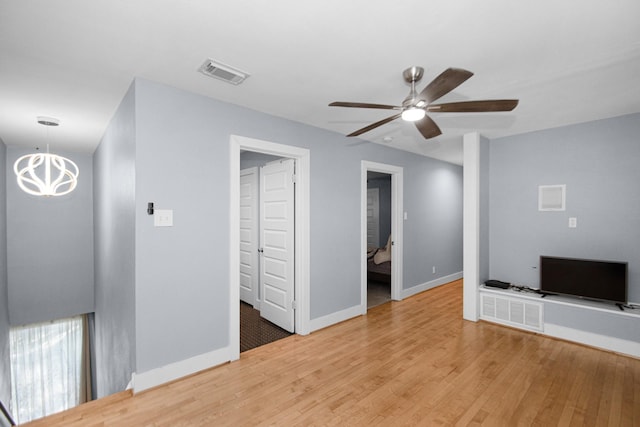 unfurnished living room with ceiling fan with notable chandelier and wood-type flooring