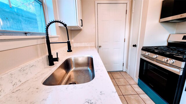 kitchen with light stone countertops, sink, light tile patterned floors, and stainless steel gas stove