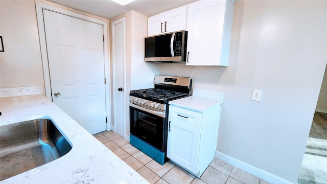 kitchen featuring sink, white cabinets, light tile patterned floors, stainless steel appliances, and light stone countertops