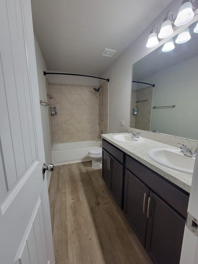 full bathroom with hardwood / wood-style flooring, toilet, tiled shower / bath, and vanity