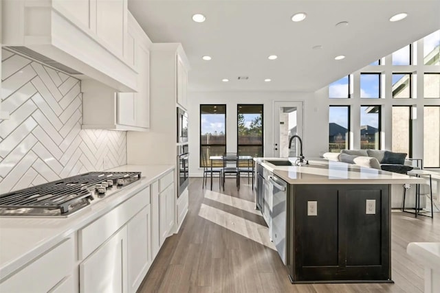 kitchen with appliances with stainless steel finishes, tasteful backsplash, a kitchen island with sink, white cabinets, and sink