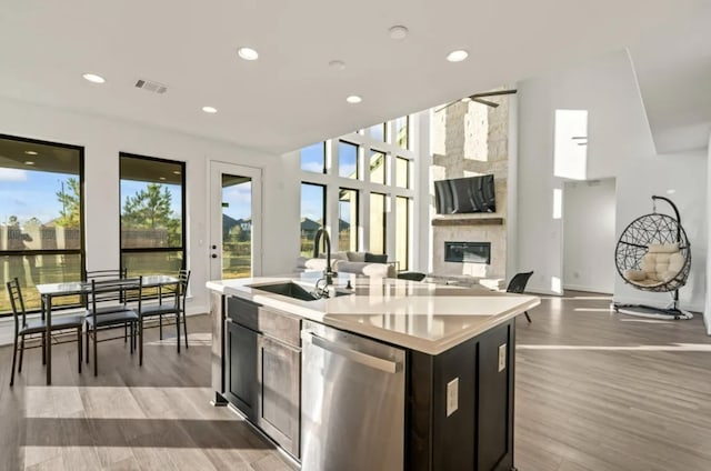 kitchen with a kitchen island with sink, light hardwood / wood-style flooring, dishwasher, and a large fireplace