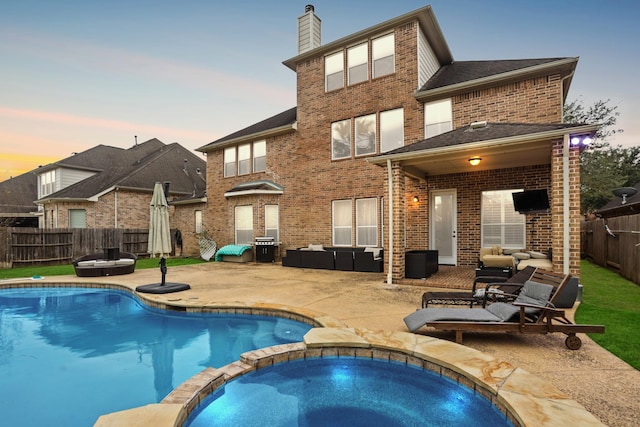 back house at dusk with a swimming pool with hot tub, an outdoor living space, and a patio