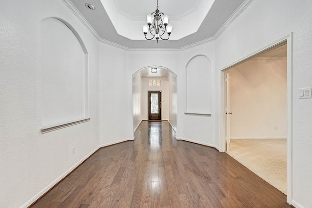 corridor featuring a chandelier, a raised ceiling, crown molding, and hardwood / wood-style floors