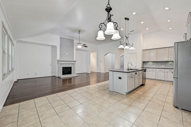 kitchen with appliances with stainless steel finishes, decorative light fixtures, tasteful backsplash, light tile patterned flooring, and a center island with sink