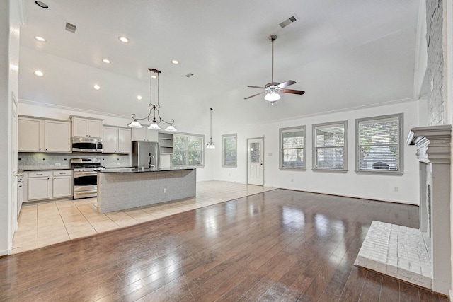 kitchen featuring appliances with stainless steel finishes, decorative backsplash, pendant lighting, a center island with sink, and lofted ceiling