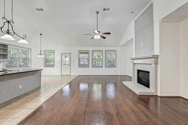 unfurnished living room featuring lofted ceiling, ceiling fan, sink, hardwood / wood-style flooring, and a brick fireplace