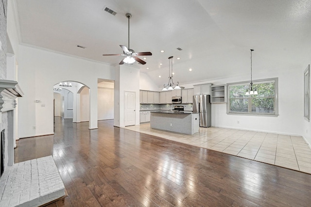 unfurnished living room featuring light wood-type flooring, ceiling fan with notable chandelier, ornamental molding, and high vaulted ceiling