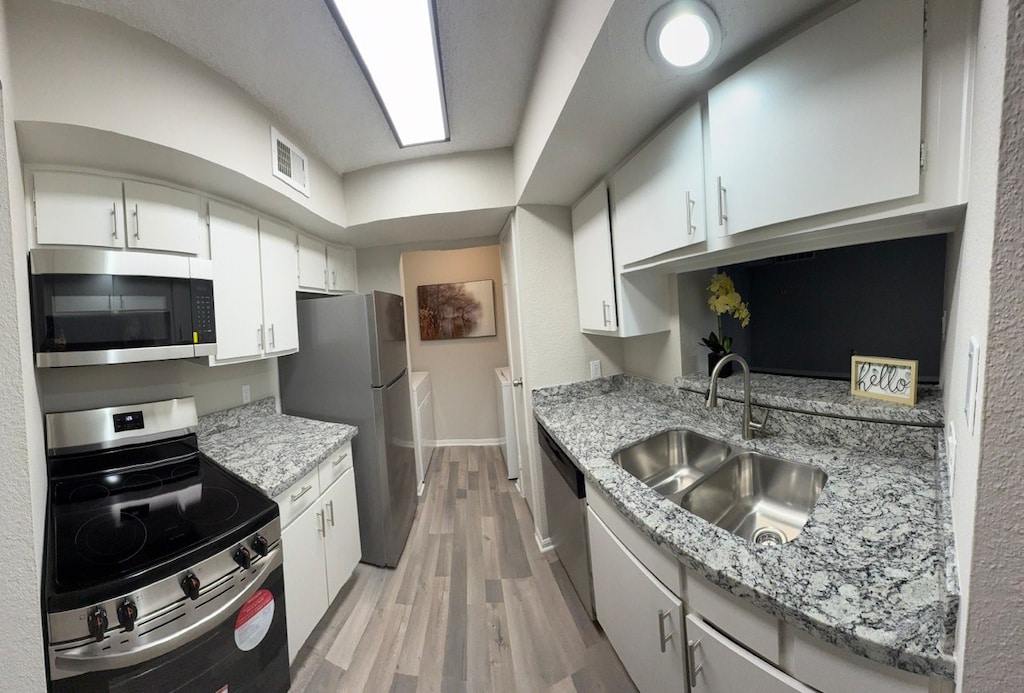 kitchen featuring light hardwood / wood-style floors, washing machine and clothes dryer, sink, white cabinets, and stainless steel appliances