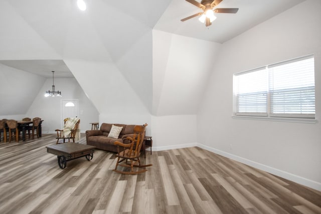 living room featuring ceiling fan with notable chandelier, light hardwood / wood-style flooring, and vaulted ceiling