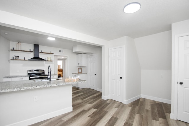 kitchen with hardwood / wood-style flooring, white cabinetry, wall chimney range hood, stainless steel range with electric stovetop, and sink